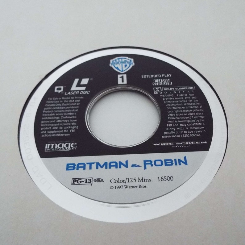 May include: A white laser disc with a black center featuring the Warner Bros. logo and the title "Batman & Robin". The disc is rated PG-13 and has a runtime of 125 minutes. The text "Color/125 Mins. 16500 &copy; 1997 Warner Bros." is printed on the disc.