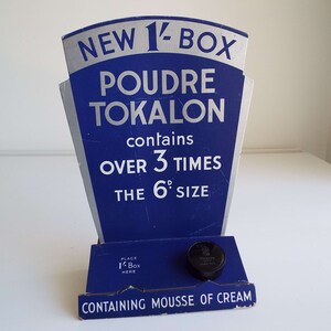 以下が含まれることがあります： 青と銀の段ボール製のディスプレイスタンドが、「ニュー1/2ボックスプードルトカロン」を宣伝し、「製品の6dサイズの3倍以上」が含まれていると記載されています。スタンドには箱を置く場所があり、「ムースオブクリーム入り」と記載されています。