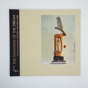 Puede incluir: Volumen 7 del libro "The Dominion of the Dream" del Museo de Arte Moderno de Nueva York. La portada presenta una fotografía de una escultura de madera con un loro posado en la parte superior.