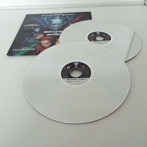 May include: Two white Blu-ray discs with a black label that reads "Batman & Robin" and a silver disc with the Warner Bros. logo. The discs are on a white surface.