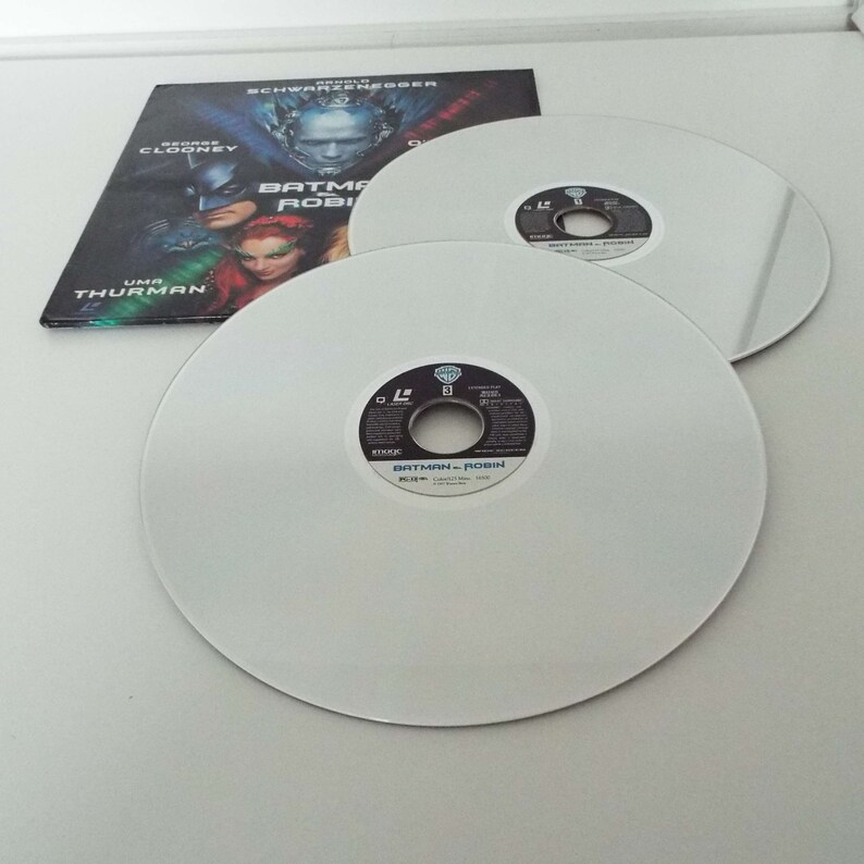 May include: Two white Blu-ray discs with a black label that reads "Batman & Robin" and a silver disc with the Warner Bros. logo. The discs are on a white surface.