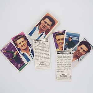 May include: A collection of vintage football trading cards featuring famous players like Stanley Matthews and Colin McDonald. The cards are printed in black and white with red and blue accents. The cards are from the Cadet Sweets series.