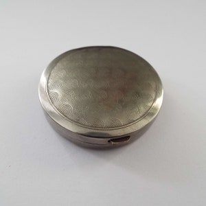 May include: A silver round compact with a wavy pattern on the lid.