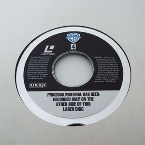 May include: A black laser disc with a silver border. The disc has a warning about copyright infringement and a note that the program material is recorded on the other side of the disc. The disc is labeled "Laser Disc" and has the number "4" printed on it.
