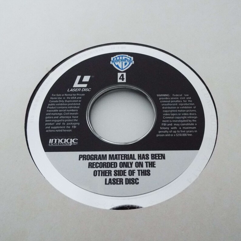 May include: A black laser disc with a silver border. The disc has a warning about copyright infringement and a note that the program material is recorded on the other side of the disc. The disc is labeled "Laser Disc" and has the number "4" printed on it.