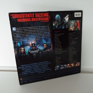 May include: Back cover of a DVD case for the movie Batman & Robin. The cover features a black and white image of Batman, Robin, and Batgirl standing in front of a frozen cityscape. The text on the cover reads "CONSISTENTLY DAZZLING. INGENIOUS. BREATHTAKING." and lists the cast and crew of the film.