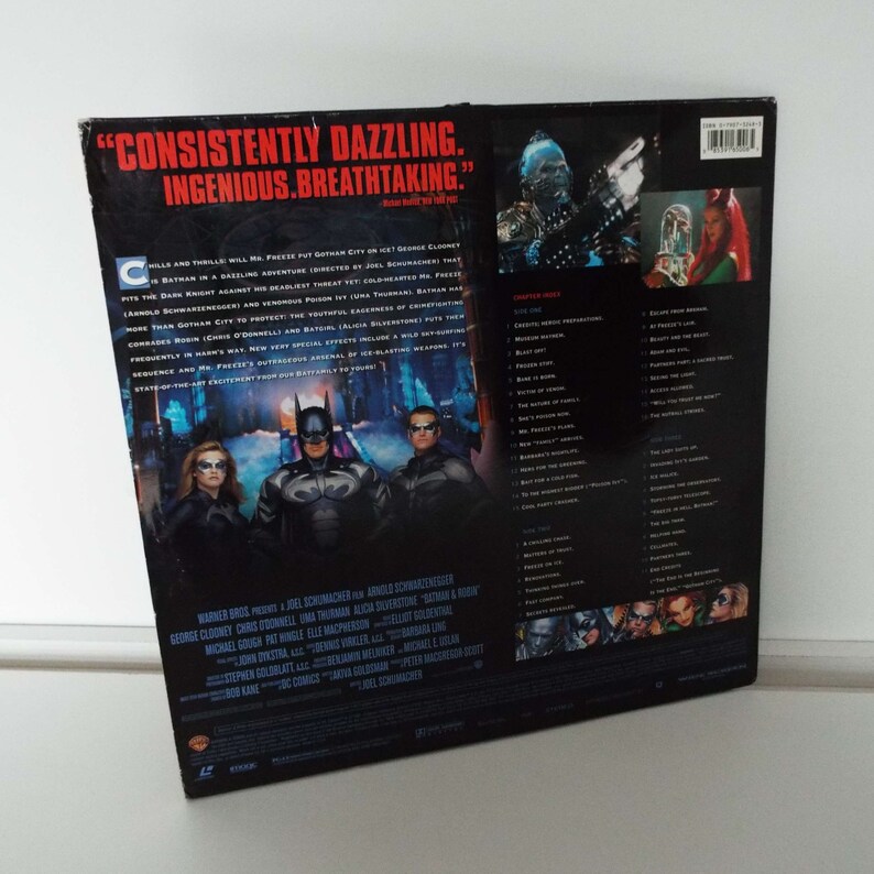 May include: Back cover of a DVD case for the movie Batman & Robin. The cover features a black and white image of Batman, Robin, and Batgirl standing in front of a frozen cityscape. The text on the cover reads "CONSISTENTLY DAZZLING. INGENIOUS. BREATHTAKING." and lists the cast and crew of the film.