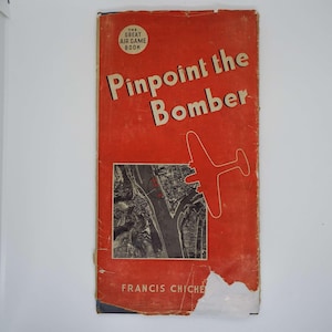 May include: The Great Air Game Book: Pinpoint the Bomber by Francis Chichester. The cover features a red background with a black and white aerial photograph of a city and a red silhouette of a bomber plane.