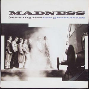 May include: Black and white photograph of a band called MADNESS, standing in front of a train. The band are waiting for the ghost train. The text (waiting for) the ghost-train is printed in purple.