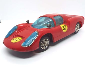 May include: A red toy race car with blue tinted windows and the number 37 in a yellow circle on the side and front. The car has black wheels and a streamlined design.