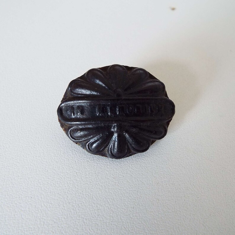 May include: Black rubber button with a flower design and the text "In the Round" embossed on it.