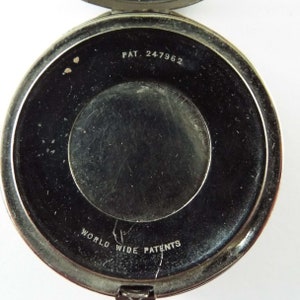 May include: The underside of a silver compact with the text "PAT. 247962" and "WORLD WIDE PATENTS" inscribed.