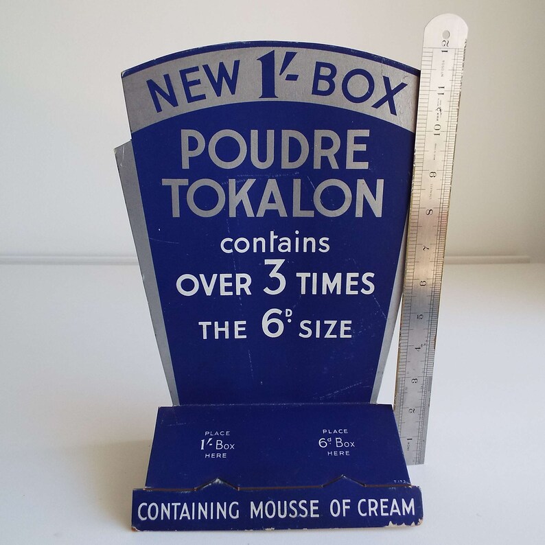 以下が含まれることがあります： 「トカロンパウダー」という製品用の青と銀の段ボール製ディスプレイスタンドです。スタンドは、6dサイズの3倍以上の量を含む新しい1 1/2ボックスサイズを宣伝しています。スタンドには、1 1/2ボックス用と6dボックス用の2つのスロットがあります。「Containing Mousse of Cream」というテキストがスタンドの下部に印刷されています。