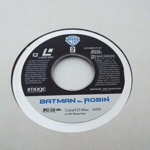 May include: A black and white laser disc with the title "Batman & Robin" in white text. The disc is rated PG-13 and has a runtime of 125 minutes. The disc is from 1997 and is a Warner Bros. production.