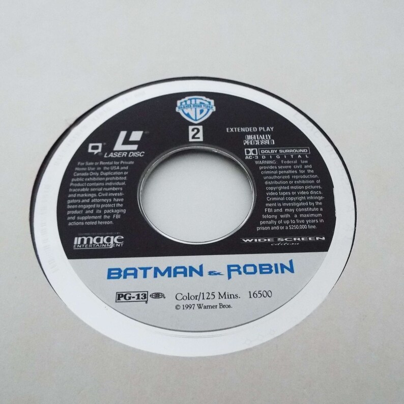 May include: A black and white laser disc with the title "Batman & Robin" in white text. The disc is rated PG-13 and has a runtime of 125 minutes. The disc is from 1997 and is a Warner Bros. production.