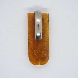 May include: A rectangular pendant with a silver-coloured bail. The pendant is a translucent amber colour with gold glitter flecks. The bail is a curved, polished metal. The pendant is approximately 3.8 cm long.