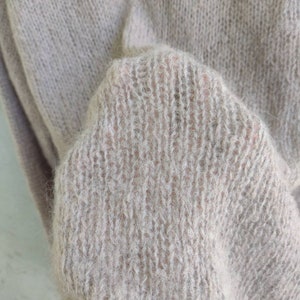 Pu&ograve; includere: Primo piano di un morbido maglione di lana color marrone chiaro con una texture pelosa.