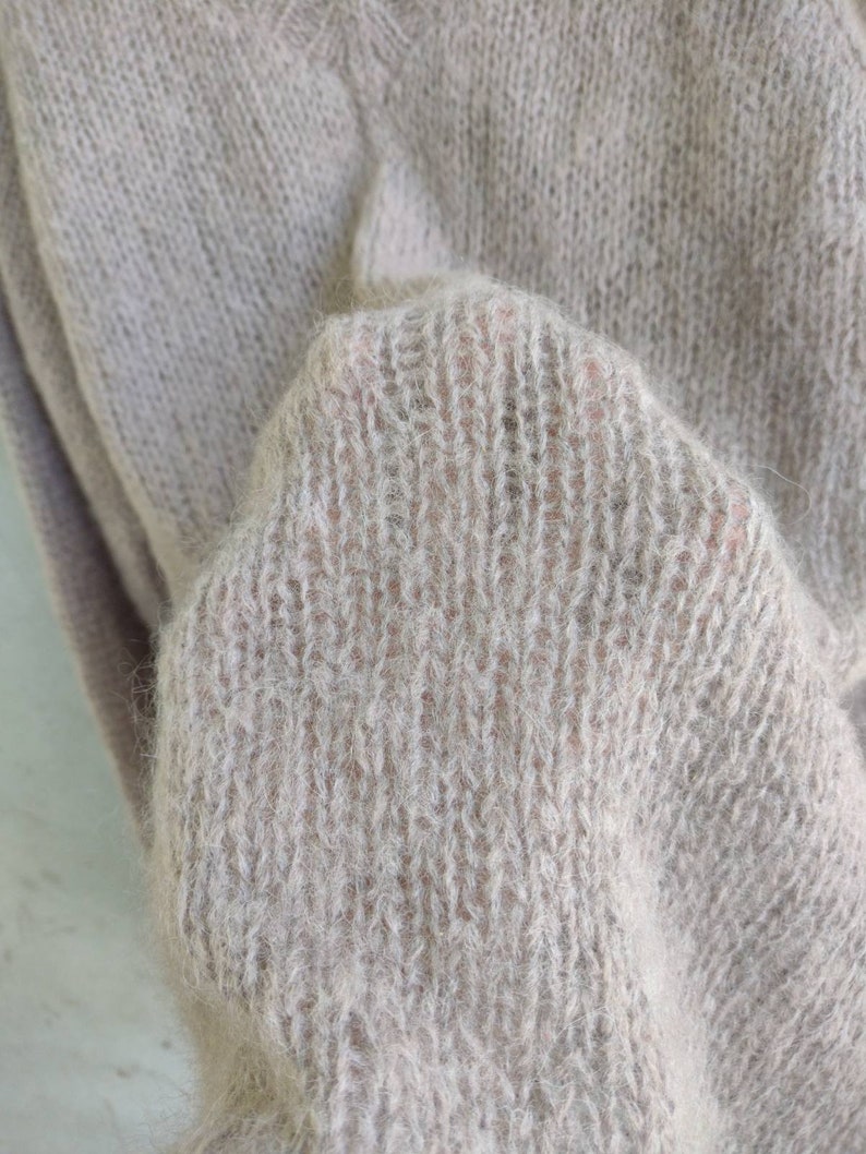 Pu&ograve; includere: Primo piano di un morbido maglione di lana color marrone chiaro con una texture pelosa.