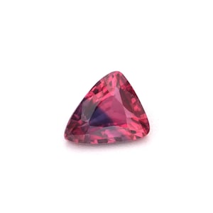 May include: A faceted, triangular gemstone with a deep pink hue and a hint of purple. The gem is set against a white background, showcasing its clarity and brilliance. The shape is a modified triangle, with one side slightly curved.