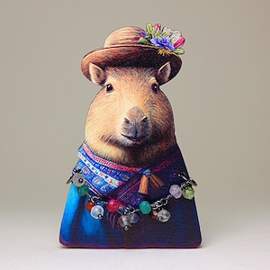 Peut inclure: Une figurine en bois de capybara portant un chapeau brun avec des fleurs, une écharpe bleue et rouge et une chaîne argentée avec des perles colorées.