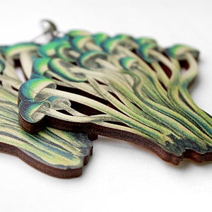 May include: A pair of wooden earrings shaped like a cluster of mushrooms. The mushrooms are painted in shades of green, white, and brown.