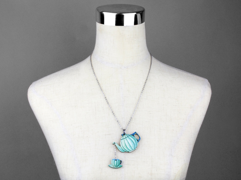 May include: A silver chain necklace with a blue and green teapot and a matching teacup pendant.