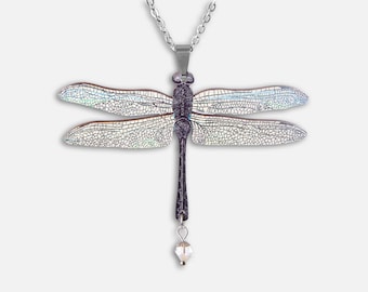 May include: A silver chain necklace with a dragonfly pendant. The dragonfly has iridescent wings and a black body. A clear crystal dangles from the dragonfly's abdomen.