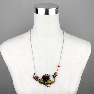May include: A silver chain necklace with a green and red dragon pendant blowing a red, orange, and yellow flame. The dragon is detailed with gold accents.