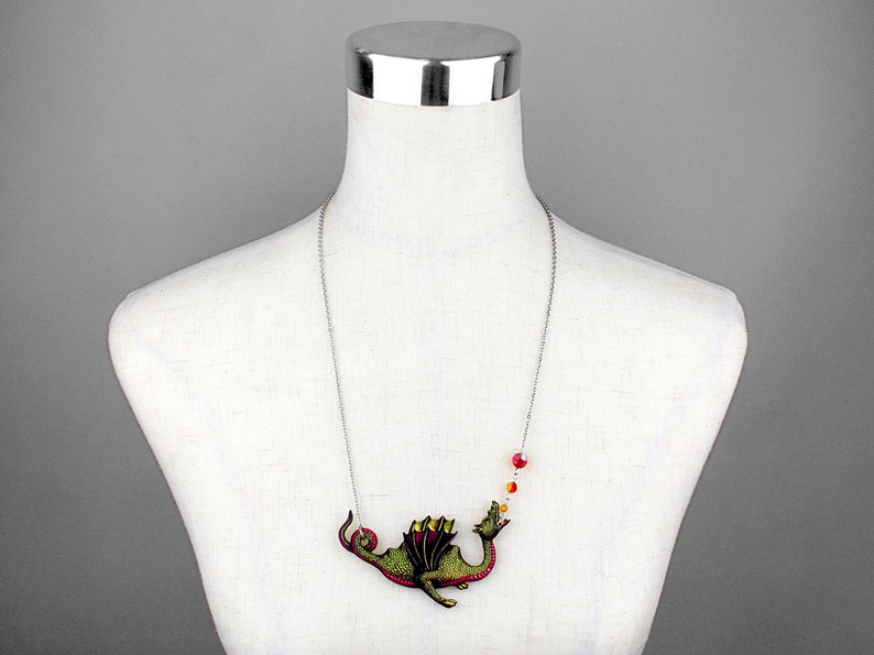 May include: A silver chain necklace with a green and red dragon pendant blowing a red, orange, and yellow flame. The dragon is detailed with gold accents.