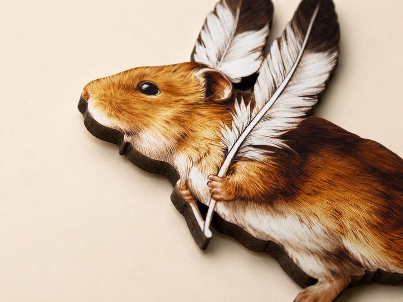 May include: A flat wooden cutout shaped like a hamster with brown and white fur. The hamster is depicted holding two large, detailed white feathers with dark brown tips that extend upwards from its body, creating a wing-like appearance.