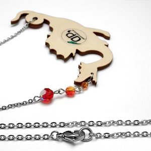 May include: A wooden dragon necklace with a silver chain and red and orange crystal beads. The dragon is cut out of wood and has a natural wood finish. The necklace is 18 inches long and has a lobster clasp closure.