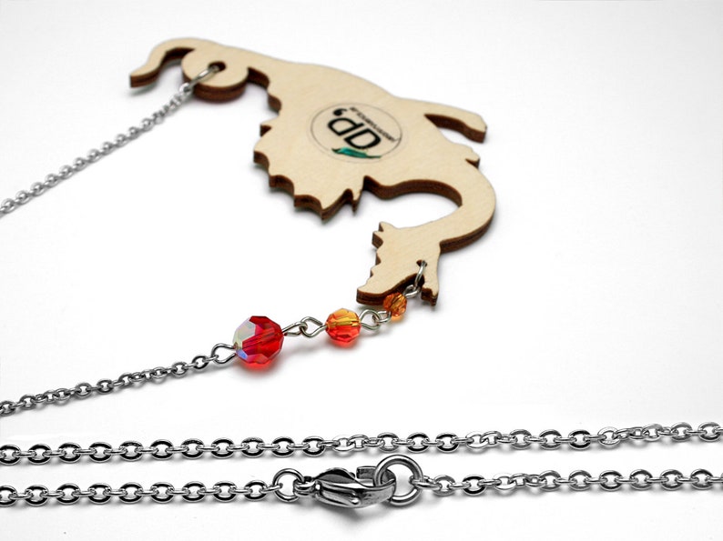 May include: A wooden dragon necklace with a silver chain and red and orange crystal beads. The dragon is cut out of wood and has a natural wood finish. The necklace is 18 inches long and has a lobster clasp closure.