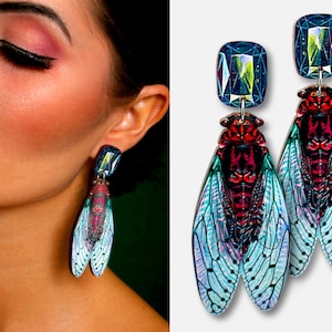 Peut inclure: Une paire de boucles d'oreilles pendantes avec un motif de cigale aux ailes bleues, vertes et rouges. Les boucles d'oreilles ont une pierre précieuse transparente et facetée en haut.