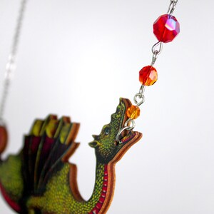 May include: A green dragon pendant necklace with red and orange crystal beads. The dragon is made of wood and has a detailed design.