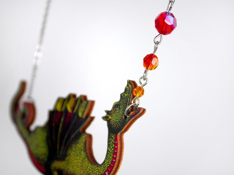 May include: A green dragon pendant necklace with red and orange crystal beads. The dragon is made of wood and has a detailed design.