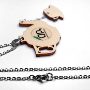 May include: A wooden teapot pendant necklace with a silver chain. The teapot has a brown wood grain finish and a small green and blue logo that says "DD".