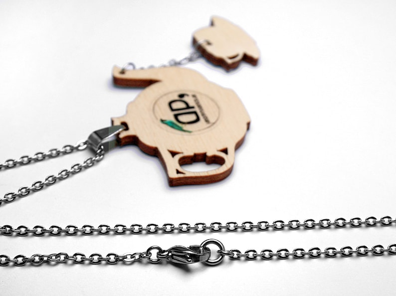 May include: A wooden teapot pendant necklace with a silver chain. The teapot has a brown wood grain finish and a small green and blue logo that says "DD".