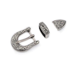 May include: Silver-toned belt buckle with an ornate floral design. The buckle is made up of three pieces: a main buckle, a strap keeper, and a tip.