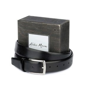 May include: A black leather belt with a silver buckle, wrapped around a wooden box with the text "Alekkss Movins" on a white label.