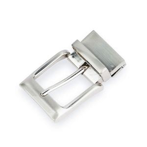 May include: A silver metal belt buckle with a smooth, brushed finish. The buckle is rectangular in shape and has a simple design.