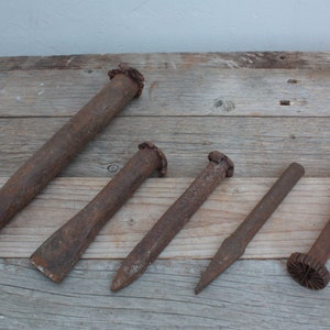May include: Five rusty metal chisels with different shapes and sizes, laid out on a wooden surface.