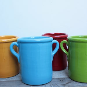 May include: Four ceramic mugs with handles, in yellow, blue, red, and green.