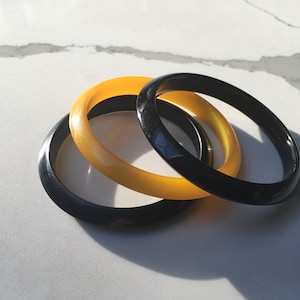 May include: Three bangle bracelets, two yellow and one black, stacked on top of each other.