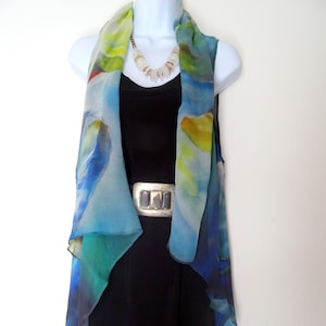 May include: A blue, green, and yellow abstract print silk scarf draped over a black sleeveless top. The scarf is worn as a vest and has a flowing, asymmetrical design.