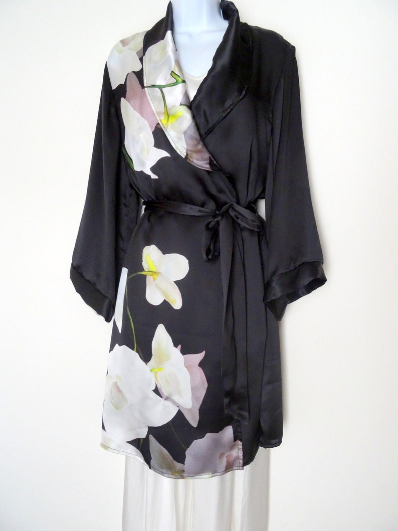 May include: A black satin robe with a white floral print. The robe has a shawl collar and a tie belt.