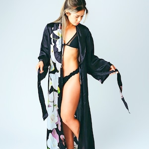 May include: A black satin robe with a floral print. The robe has long sleeves and a tie belt. The model is wearing a black bra and underwear.