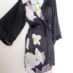 May include: A black satin robe with a floral print of white orchids. The robe has a shawl collar and a tie belt.