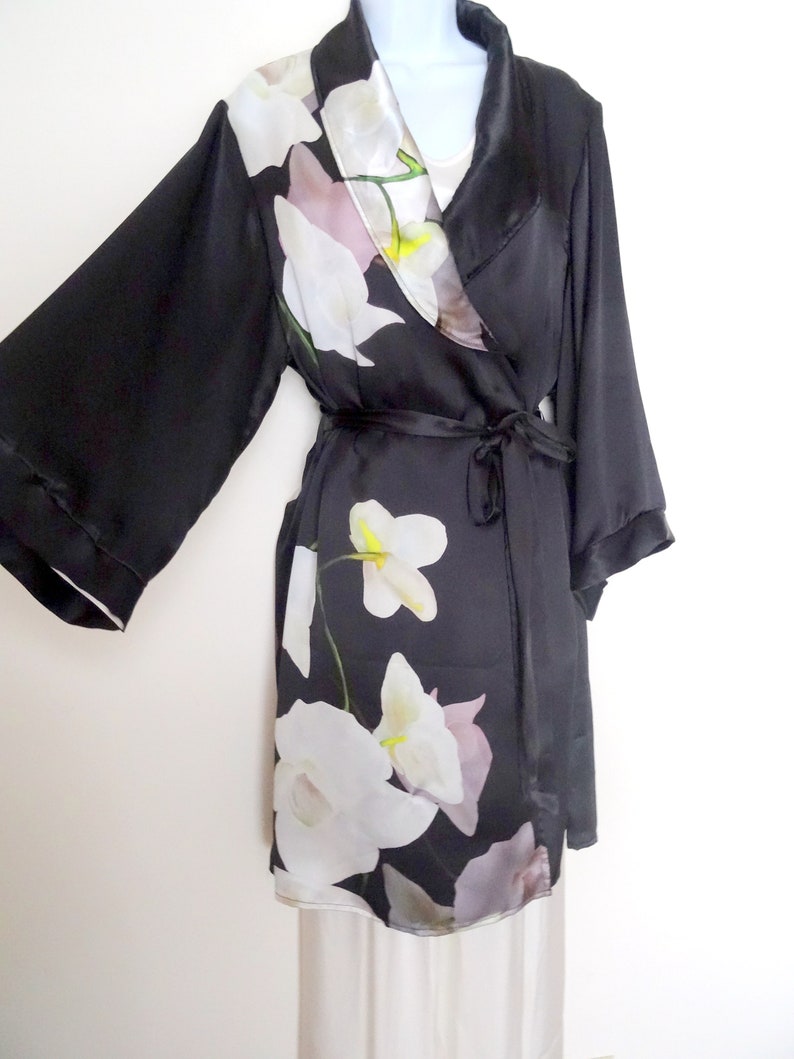 May include: A black satin robe with a floral print of white orchids. The robe has a shawl collar and a tie belt.