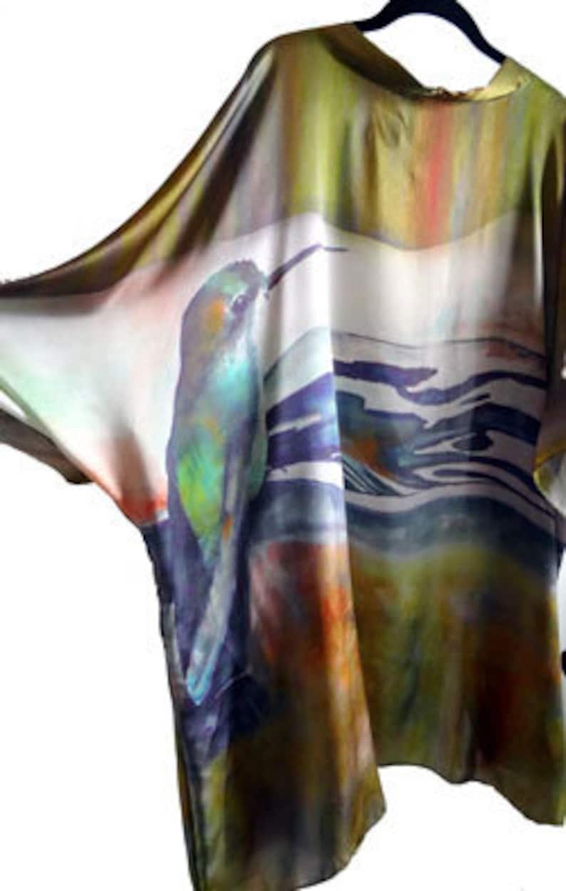 Pu&ograve; includere: Una blusa di seta fluida con un designo astratto colorato che presenta un uccello e motivi acquatici. La blusa &egrave; in tonalit&agrave; di verde, blu, giallo e arancione.