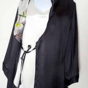 May include: A black satin robe with a white floral print on the collar. The robe has a tie at the waist and long sleeves.